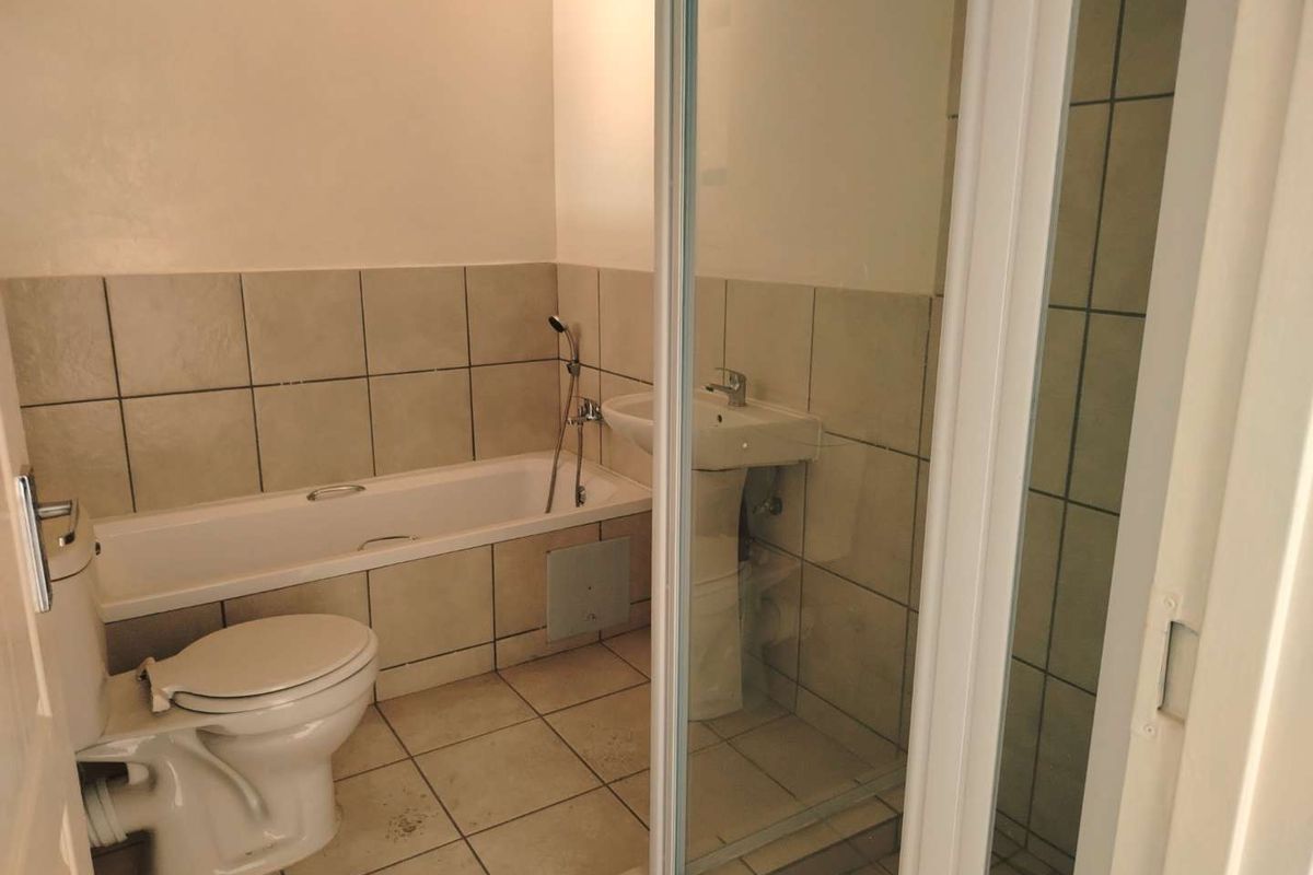 A functional bathroom featuring a bathtub, pedestal sink, toilet, and a separate shower enclosure with neutral ceramic tiling throughout.