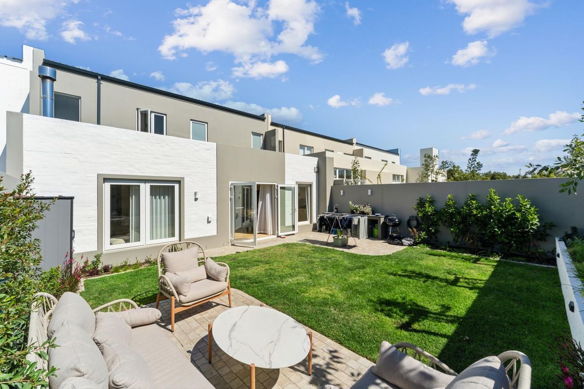 A well-maintained rear garden featuring a paved patio area, manicured lawn, and direct access to the home through double glass doors.
