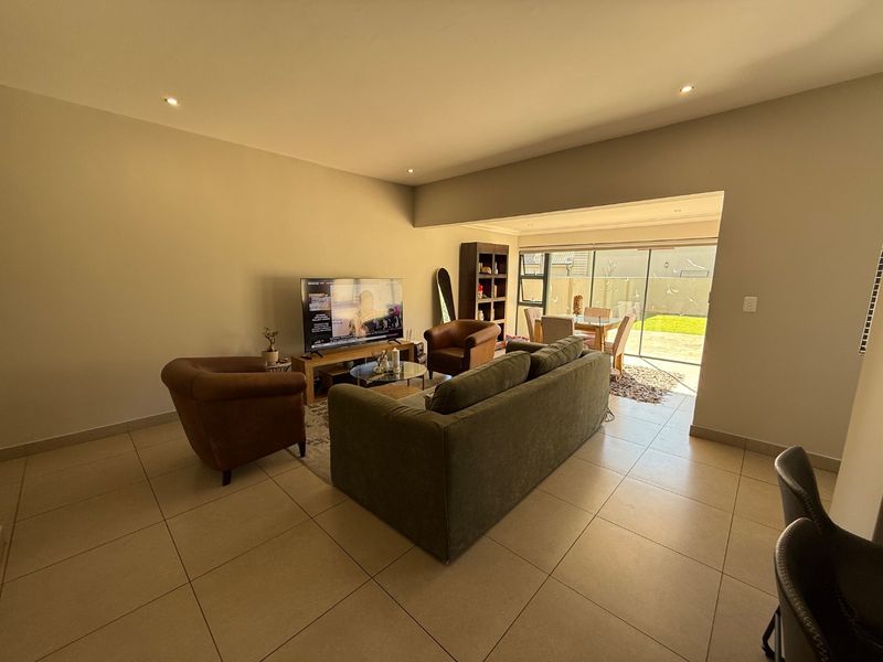 Spacious open-plan living area featuring neutral tiled flooring, recessed lighting, and large sliding glass doors providing seamless access to the rear patio and garden.