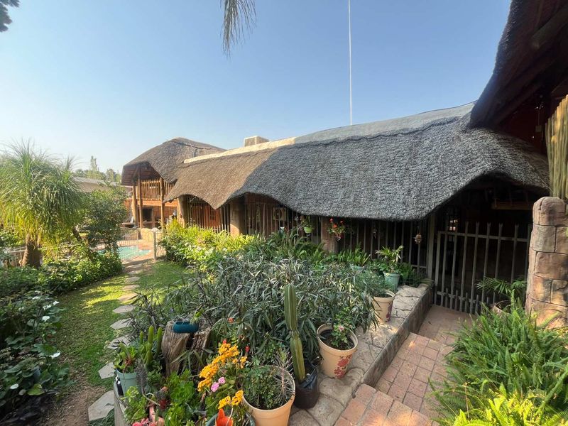 Rear view of the property featuring a traditional thatch roof, stone accents, brick pathways, and a glimpse of the swimming pool area.