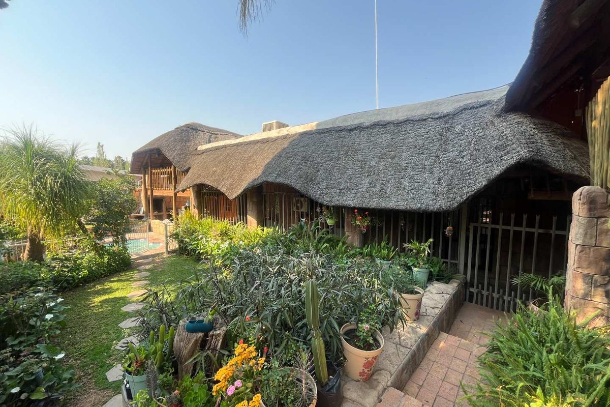 Rear view of the property featuring a traditional thatch roof, stone accents, brick pathways, and a glimpse of the swimming pool area.