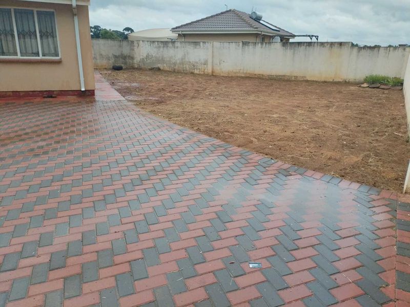 A rear exterior view featuring a paved patio area and a large, unlandscaped garden space enclosed by a boundary wall.