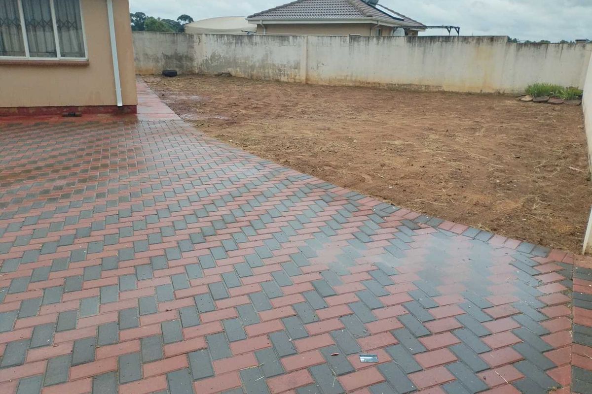 A rear exterior view featuring a paved patio area and a large, unlandscaped garden space enclosed by a boundary wall.