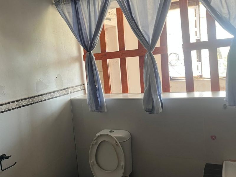 A functional bathroom featuring a toilet, vanity basin, and tiled finishes, currently requiring cosmetic attention to the wall surfaces.