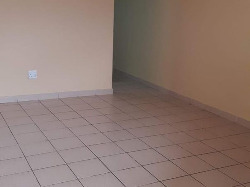 An empty living room featuring neutral ceramic floor tiles and an arched doorway leading to an adjacent space.