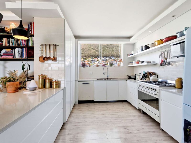 Modern, well-appointed kitchen featuring white cabinetry, quartz countertops, subway tile backsplash, gas hob, and integrated appliances with a view of the surrounding area.