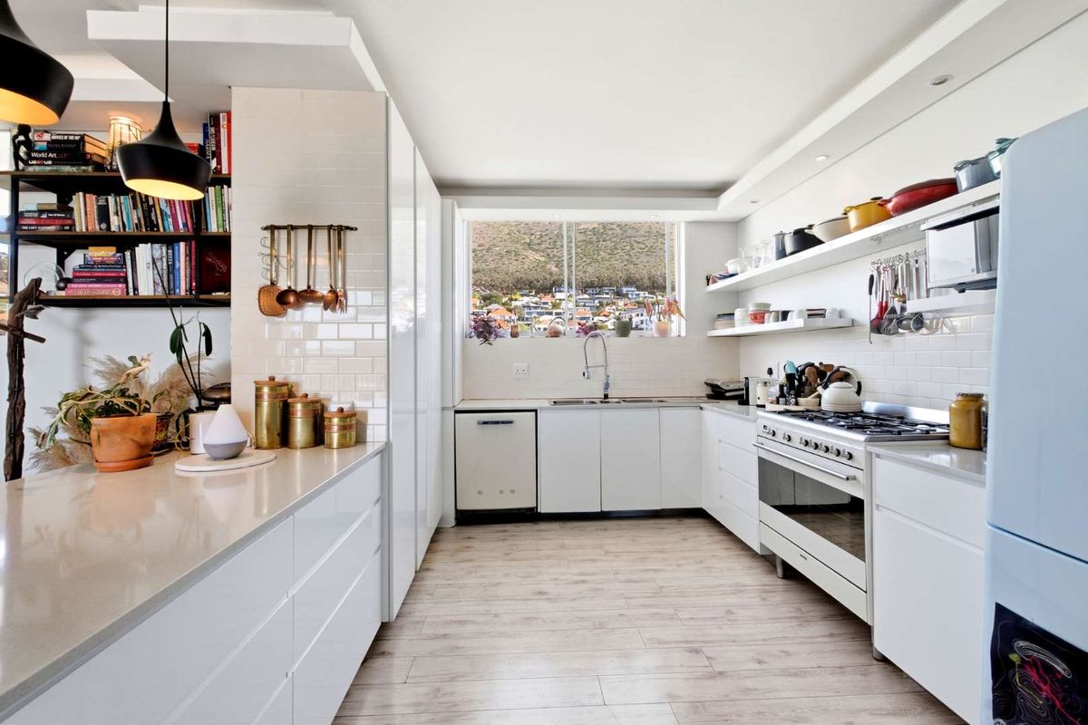Modern, well-appointed kitchen featuring white cabinetry, quartz countertops, subway tile backsplash, gas hob, and integrated appliances with a view of the surrounding area.