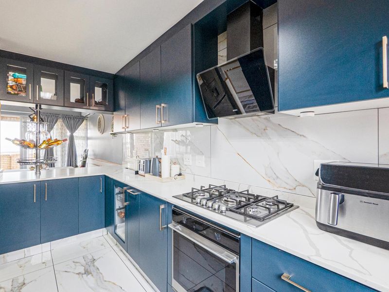 Modern kitchen featuring navy blue cabinetry, marble-look quartz countertops, high-end gas hob, integrated oven, and sleek porcelain flooring.