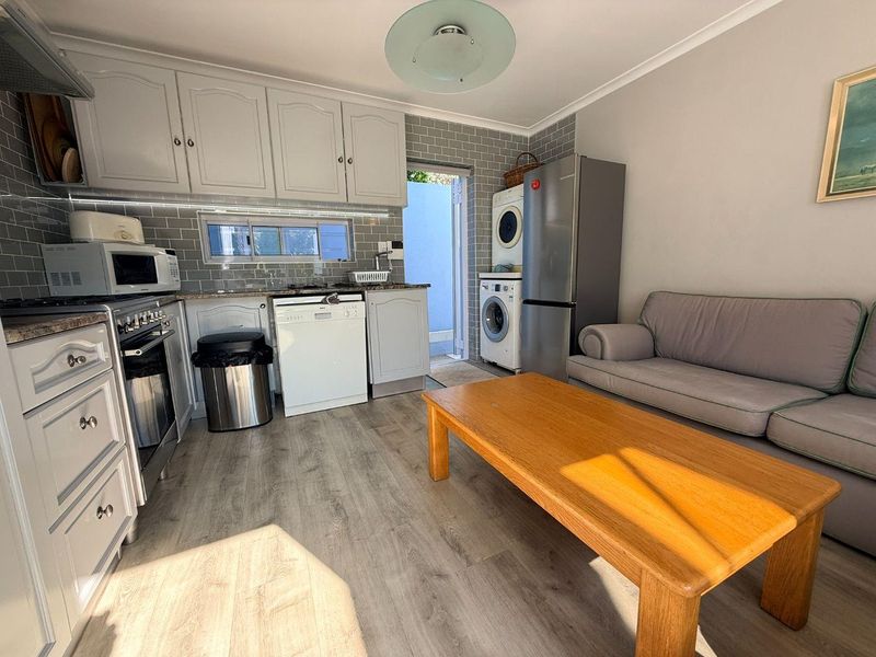Open-plan kitchen and living area featuring grey cabinetry, subway tile backsplash, and laminate wood flooring with direct access to an outdoor space.