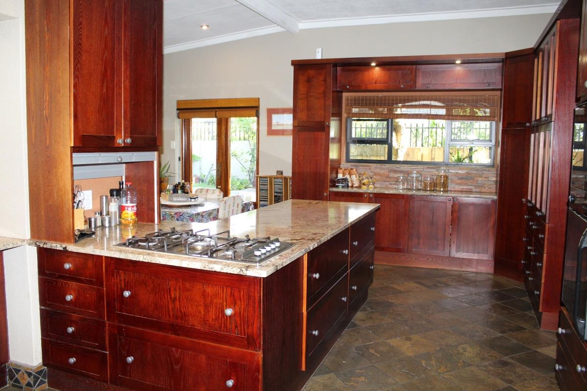Spacious kitchen featuring dark wood cabinetry, granite countertops, a central island with a built-in gas hob, and slate tile flooring.