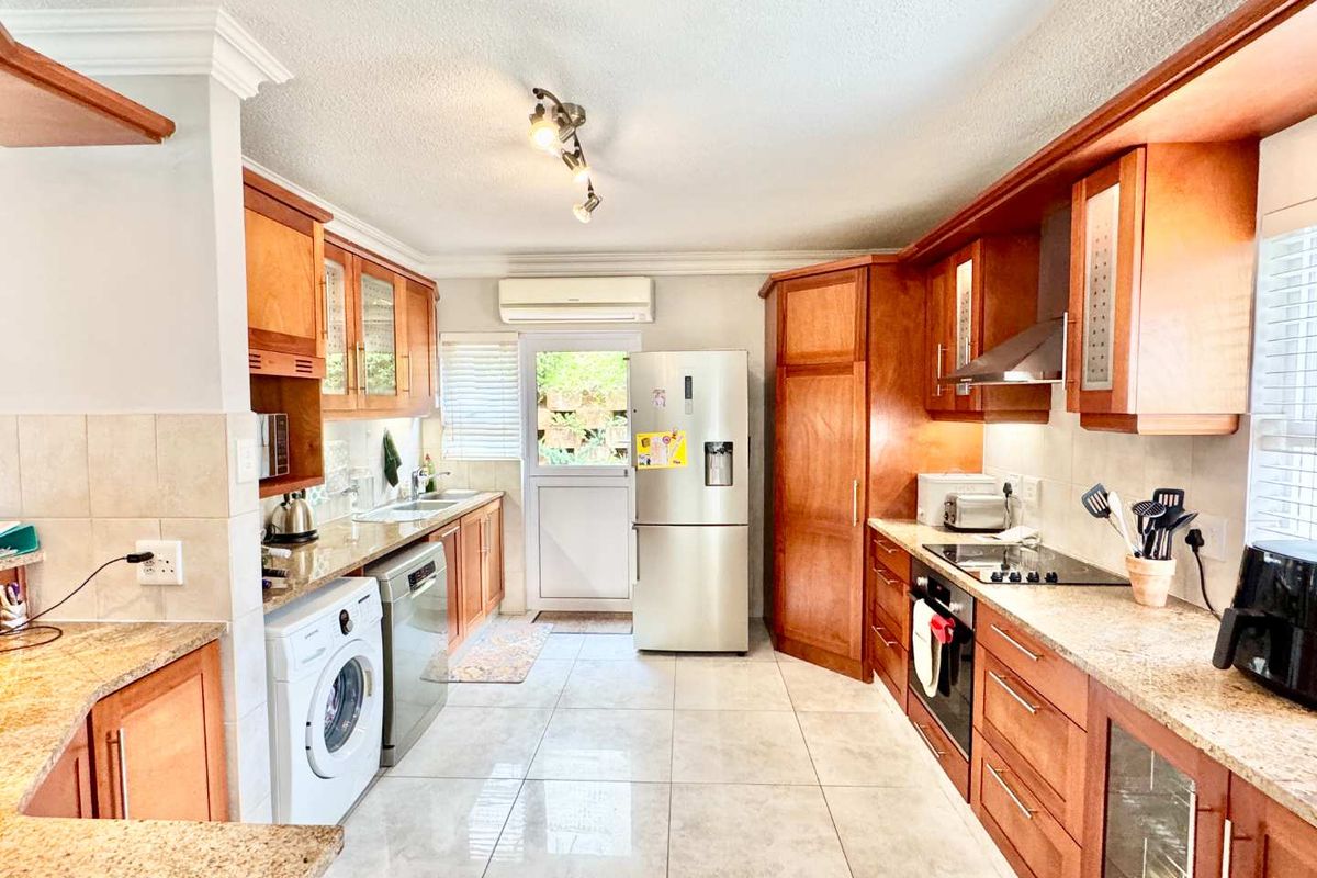 A functional kitchen featuring warm-toned wooden cabinetry, granite countertops, integrated appliances, and tiled flooring with direct access to the exterior.