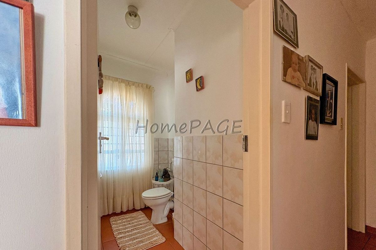 A view into a functional bathroom featuring tiled walls, a toilet, and a window with privacy curtains.