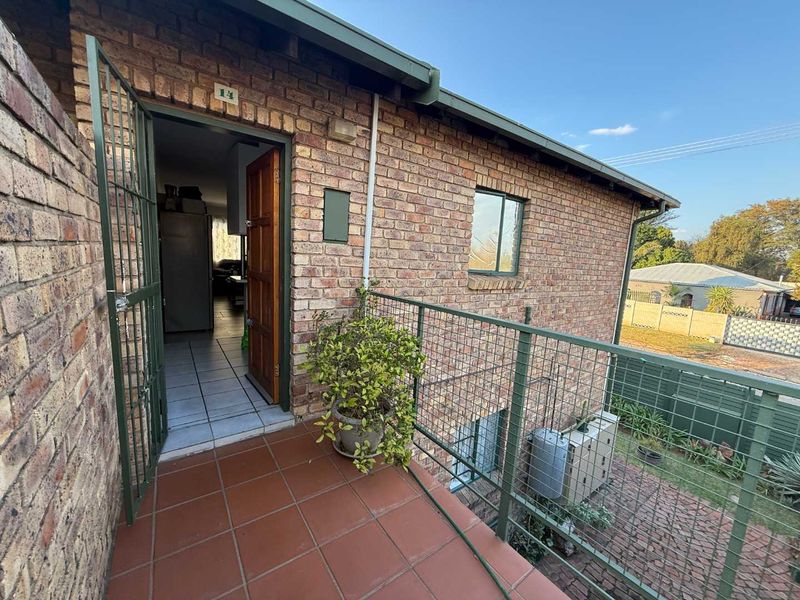 An elevated balcony with tiled flooring, metal security gate, and balustrade, providing access to the apartment entrance with views of the surrounding property.