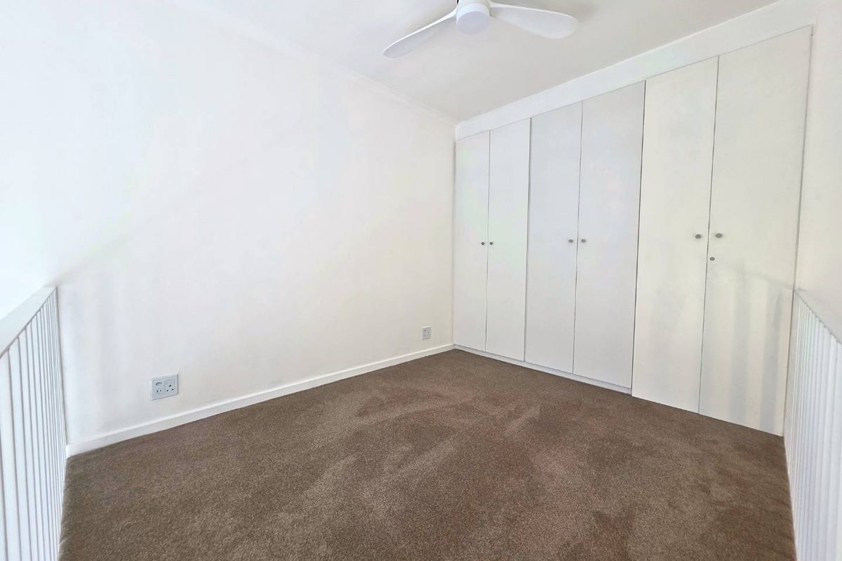 A bright, empty bedroom featuring neutral carpeting, a ceiling fan, and ample built-in cupboard storage.