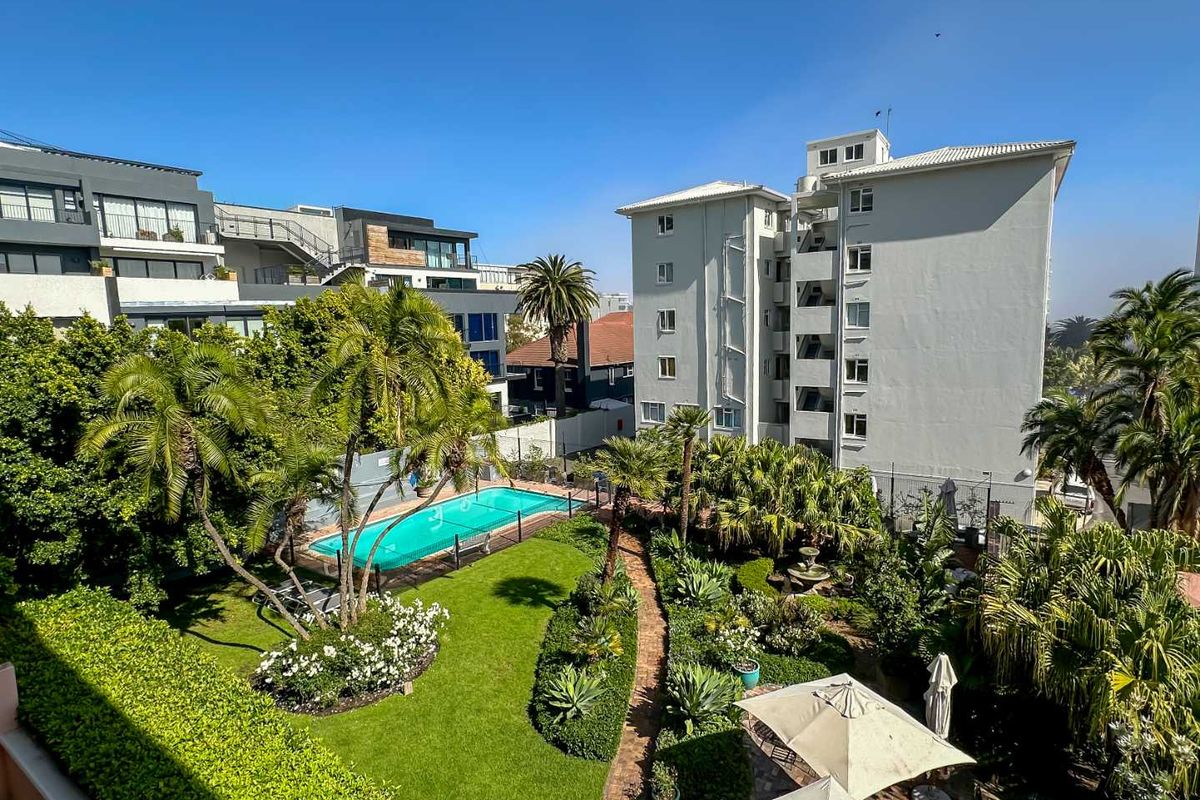 Elevated view of a well-maintained apartment complex garden featuring a swimming pool, lush landscaping, and paved pathways.