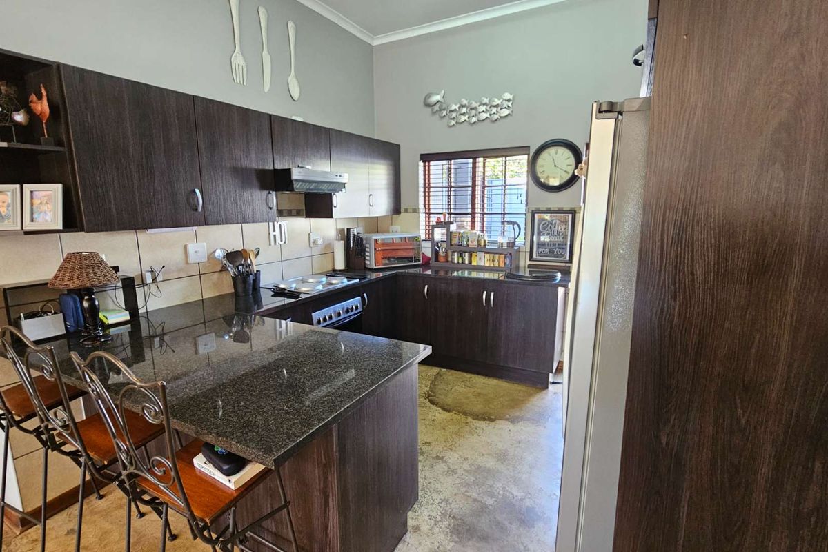 A functional kitchen featuring dark wood cabinetry, granite countertops, a breakfast bar, and a built-in hob with an extractor fan.