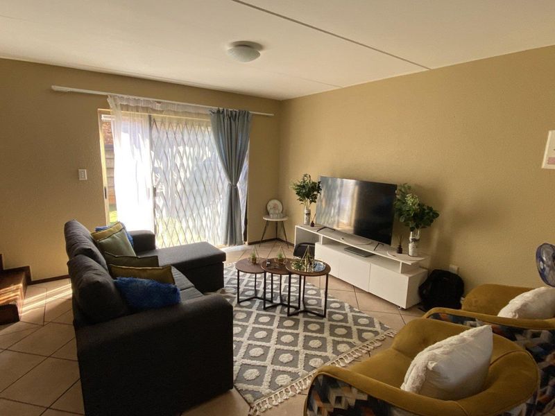A living room featuring tiled flooring, a sliding glass door with a security gate, and an adjacent staircase leading to the upper level.