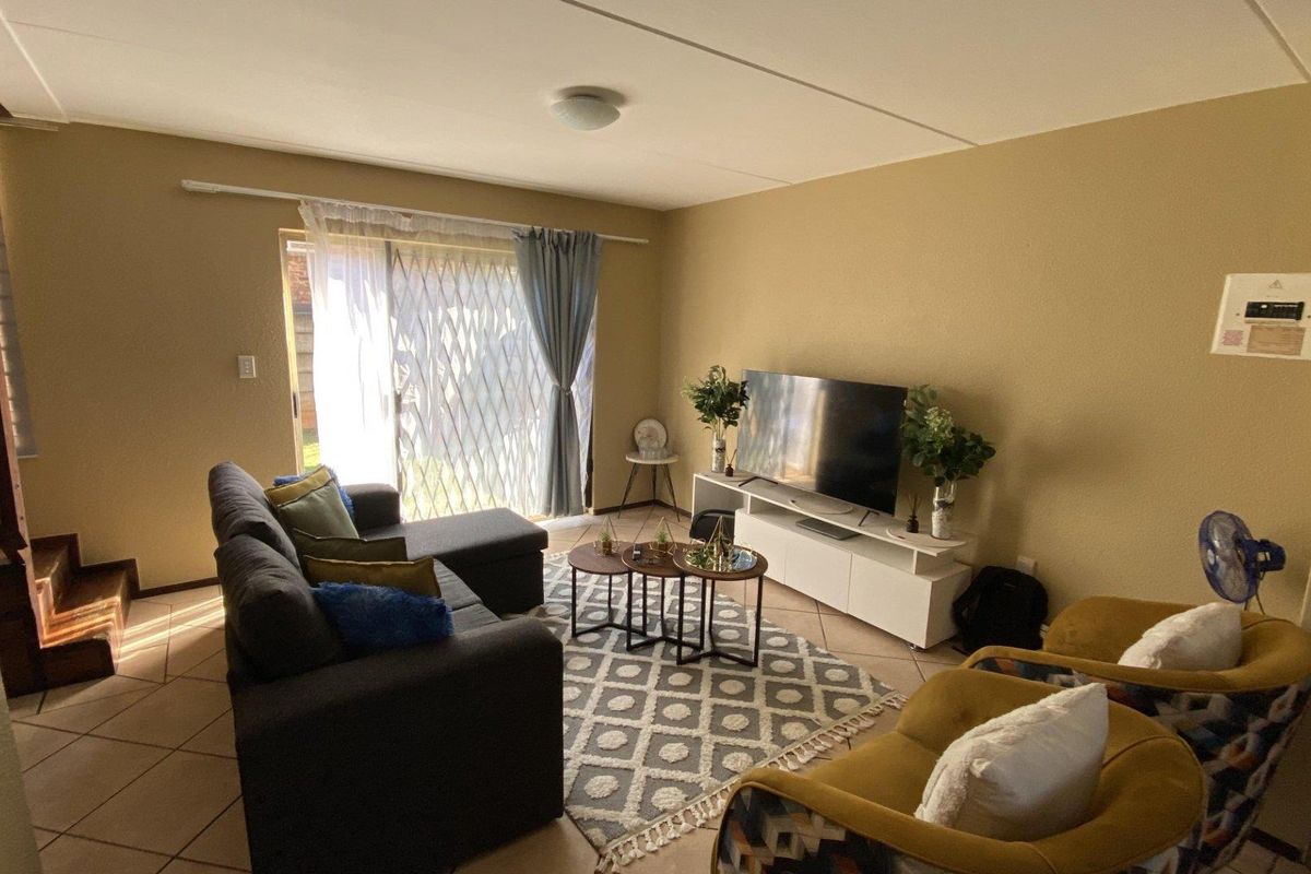 A living room featuring tiled flooring, a sliding glass door with a security gate, and an adjacent staircase leading to the upper level.