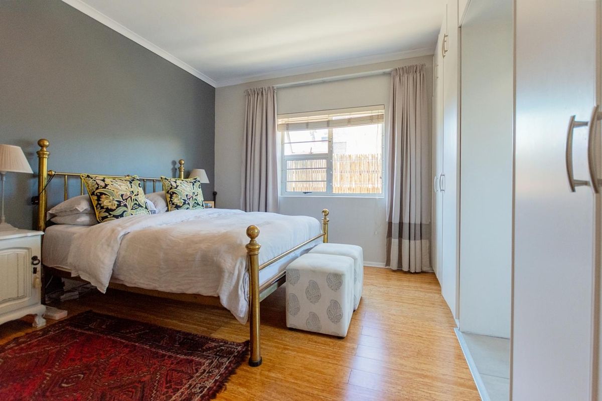 A well-maintained bedroom featuring built-in wardrobes, laminate flooring, and a large window providing natural light.