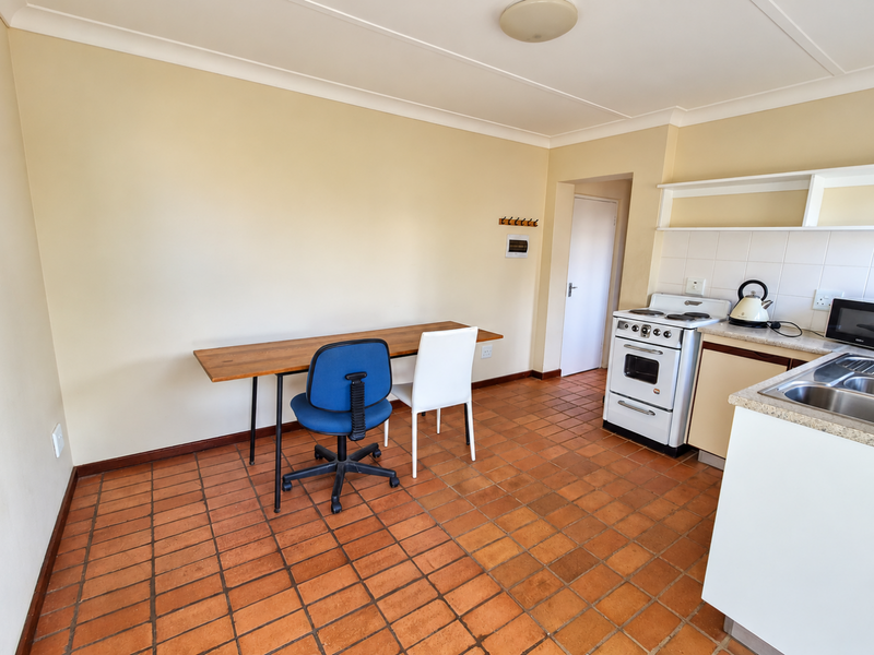 A functional kitchen featuring terracotta floor tiles, a freestanding stove, stainless steel sink, and built-in cabinetry with a tiled backsplash.