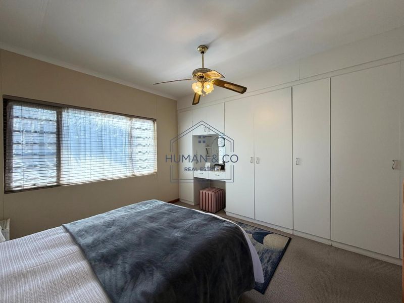 A bedroom featuring neutral walls, carpeted flooring, a ceiling fan, and extensive built-in cabinetry with an integrated vanity area.