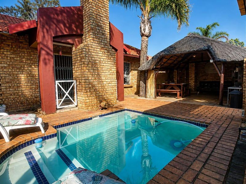 Outdoor entertainment area featuring a swimming pool and a traditional thatched lapa, set within a private brick-paved courtyard.