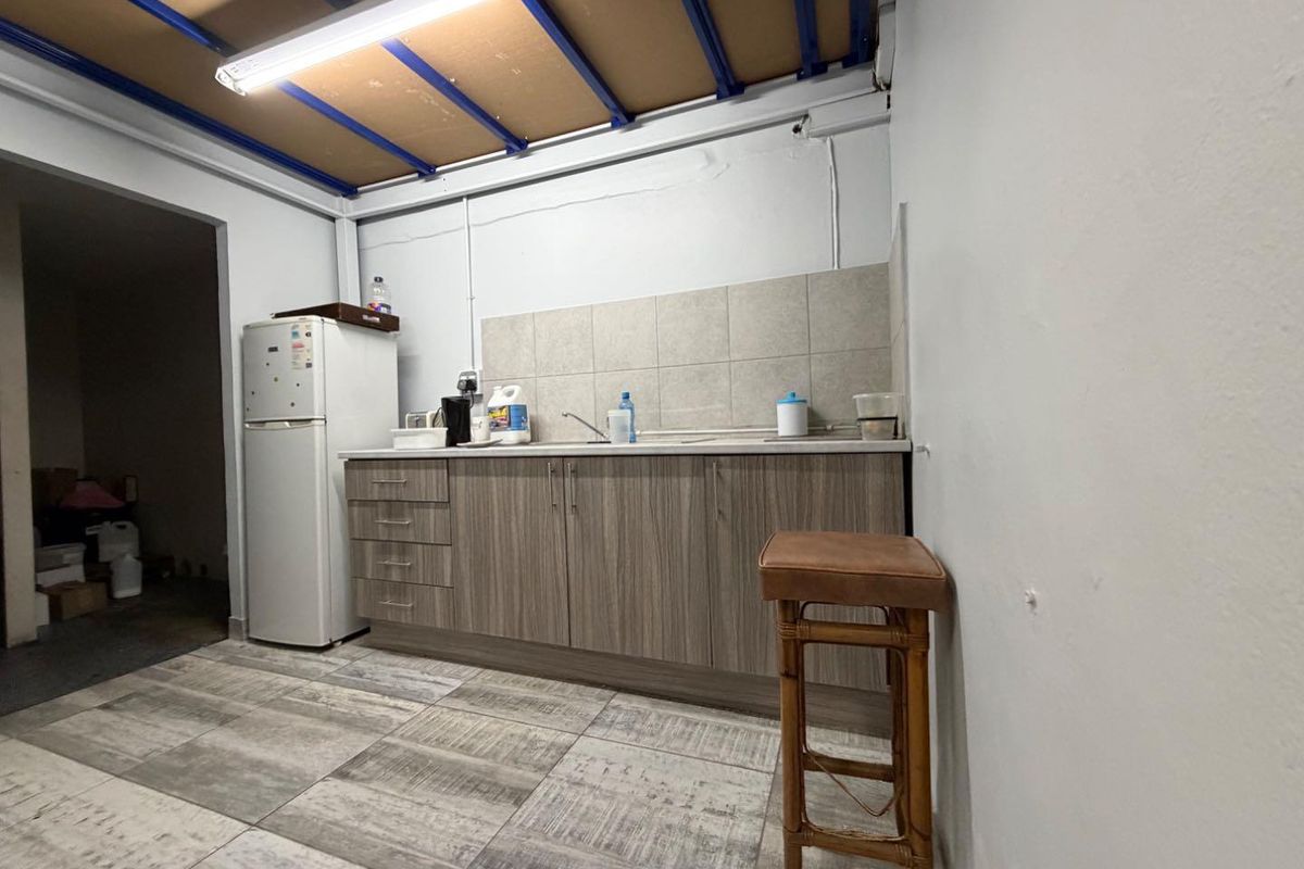 A functional kitchenette featuring wood-look cabinetry, tiled backsplash, sink, and durable tiled flooring with exposed industrial-style ceiling beams.