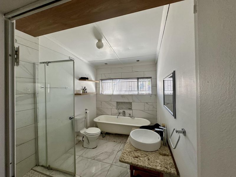 A functional bathroom featuring a freestanding bathtub, glass-enclosed shower, vessel sink on a granite vanity, and modern marble-look wall and floor tiling.