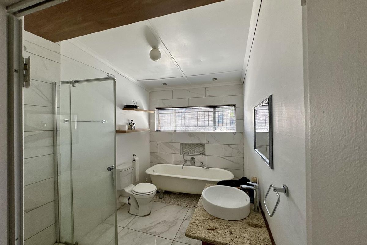 A functional bathroom featuring a freestanding bathtub, glass-enclosed shower, vessel sink on a granite vanity, and modern marble-look wall and floor tiling.