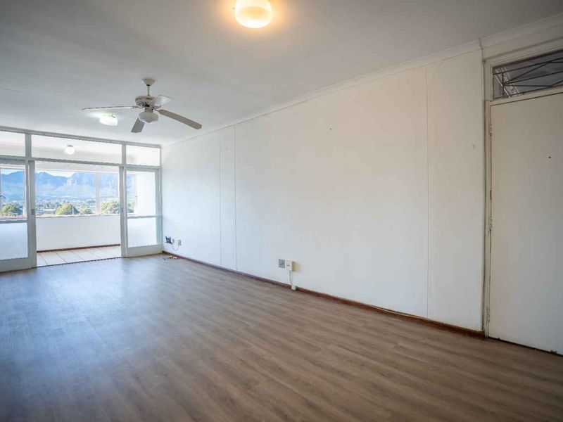 Spacious, empty living area featuring laminate flooring, a ceiling fan, and large sliding glass doors leading to a balcony with mountain views.