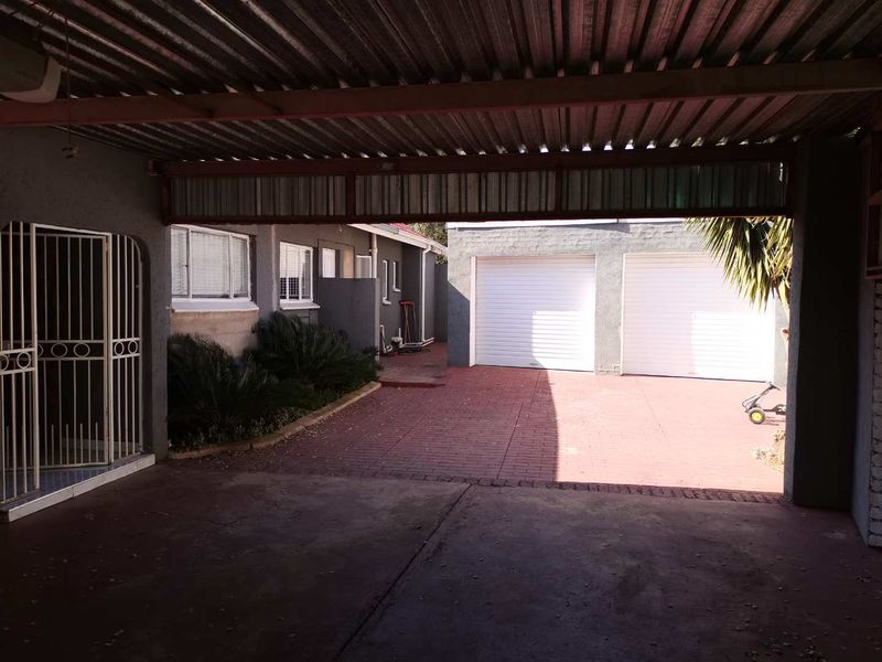 Rear exterior view featuring a covered patio area, paved driveway, and a double garage with white roller doors.