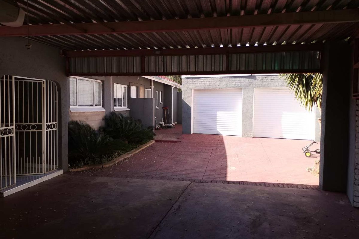 Rear exterior view featuring a covered patio area, paved driveway, and a double garage with white roller doors.