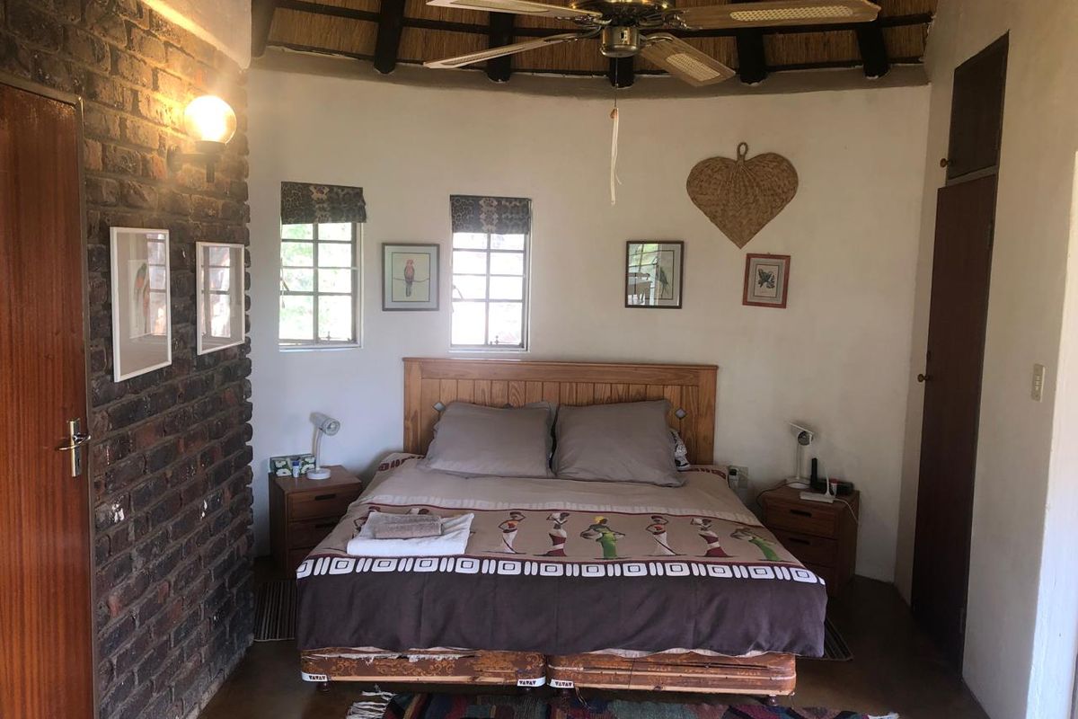 A rustic bedroom featuring a thatched roof, exposed brick wall, and tiled flooring, creating a warm and traditional atmosphere.
