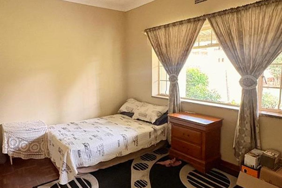 A bedroom featuring original parquet flooring, large windows allowing natural light, and a neutral wall finish.