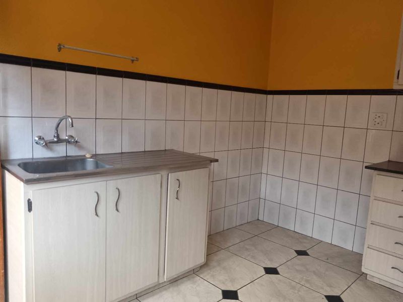 A functional kitchen area featuring tiled walls, a stainless steel sink, and built-in cabinetry, offering a blank canvas for modern renovation.