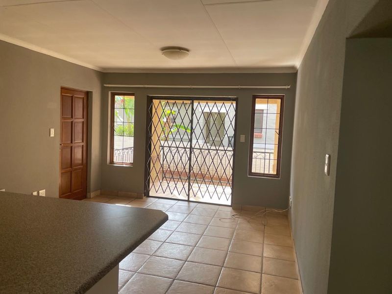 An open-plan living area featuring ceramic tile flooring, a sliding glass door with security gate, and access to an outdoor space.