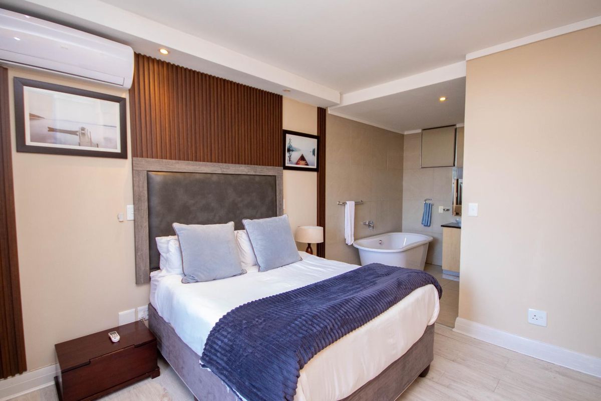 A well-appointed bedroom featuring a timber slat accent wall, split-system air conditioning, and an open-plan ensuite with a modern freestanding bathtub.