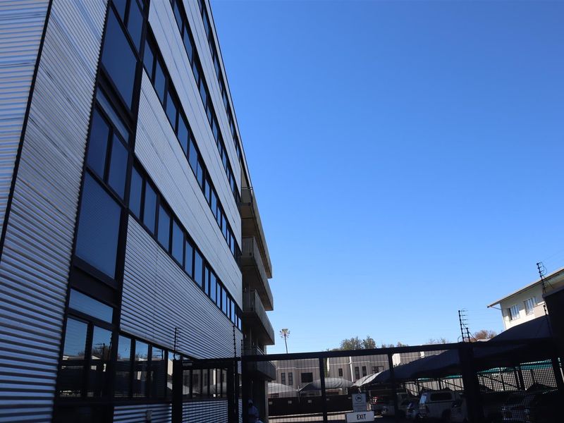Rear view of a multi-story office building featuring corrugated metal cladding, large windows, and a secure gated parking area.