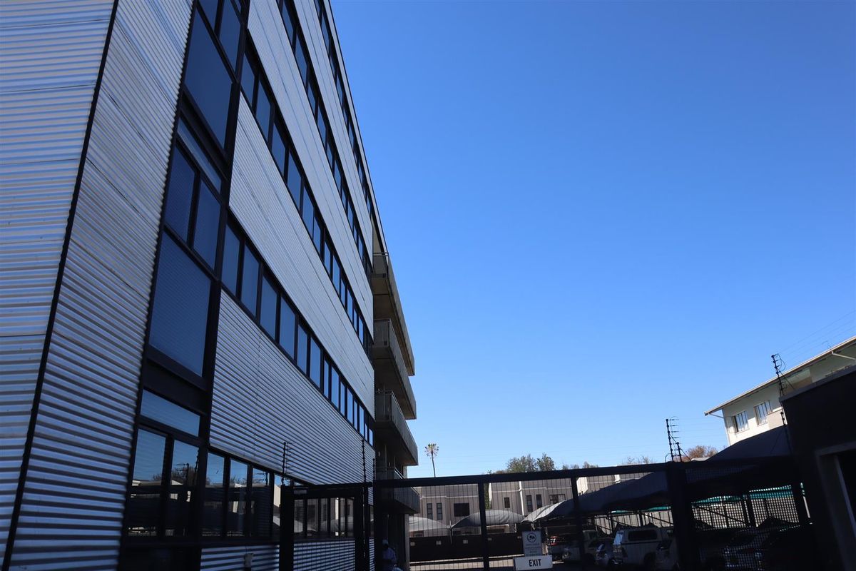 Rear view of a multi-story office building featuring corrugated metal cladding, large windows, and a secure gated parking area.