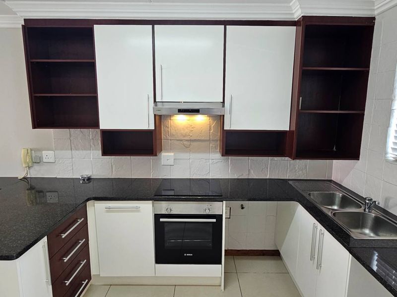A clean, functional kitchen featuring dark granite countertops, white and dark wood cabinetry, a built-in oven, electric hob, and a double stainless steel sink.