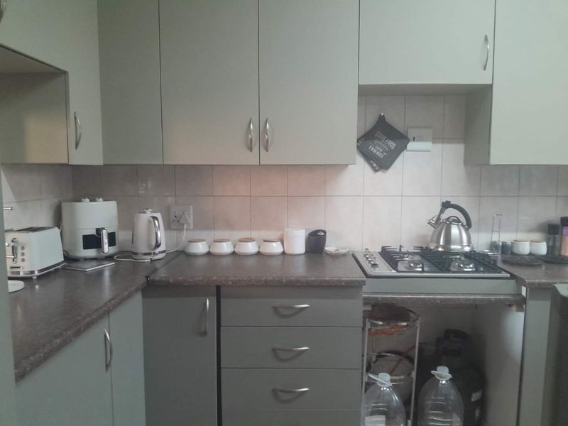 A functional kitchen featuring grey cabinetry, laminate countertops, a gas hob, and tiled backsplash, offering a practical workspace for daily cooking.