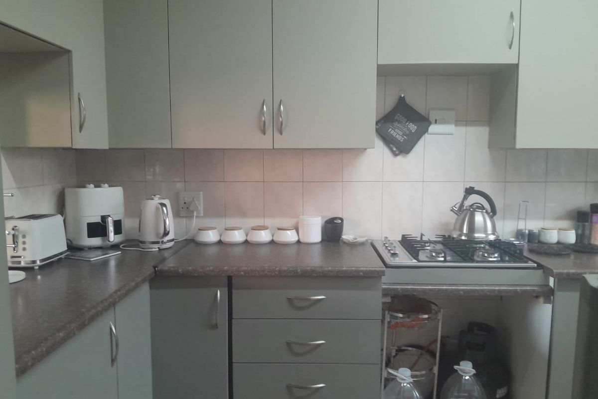 A functional kitchen featuring grey cabinetry, laminate countertops, a gas hob, and tiled backsplash, offering a practical workspace for daily cooking.