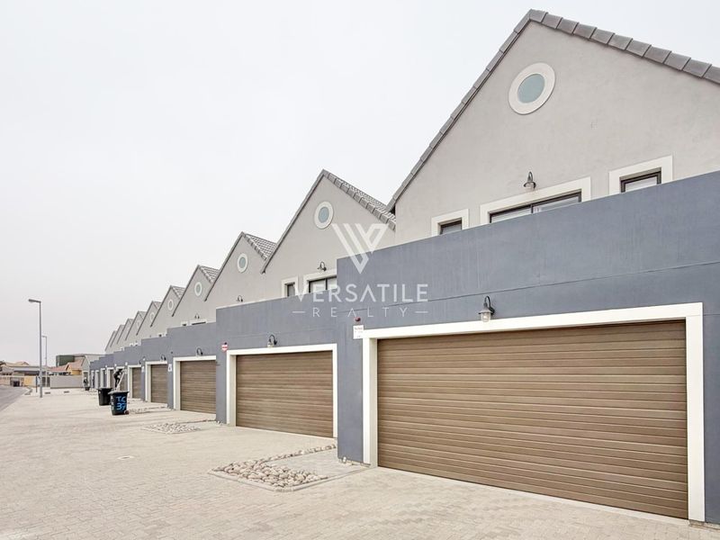 A row of modern townhouse units featuring uniform garage doors, paved driveway access, and distinctive gabled roof architecture.