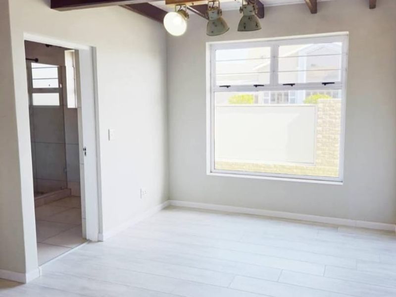 A bright, empty bedroom featuring exposed timber ceiling beams, modern light-toned laminate flooring, and direct access to an en-suite bathroom.