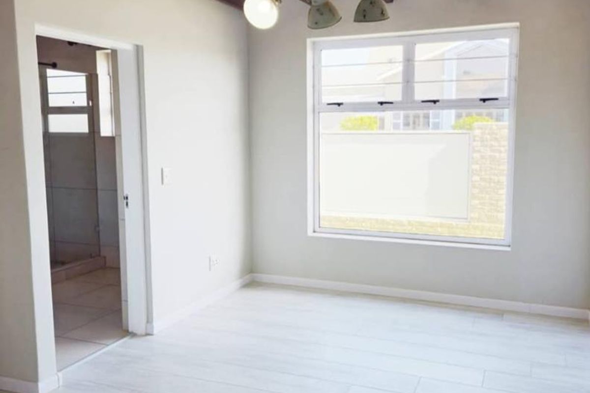A bright, empty bedroom featuring exposed timber ceiling beams, modern light-toned laminate flooring, and direct access to an en-suite bathroom.