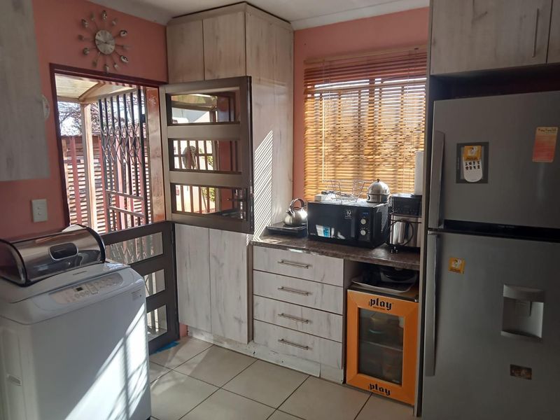 A functional kitchen area featuring built-in cabinetry, laminate countertops, tiled flooring, and direct access to the exterior through a security gate.