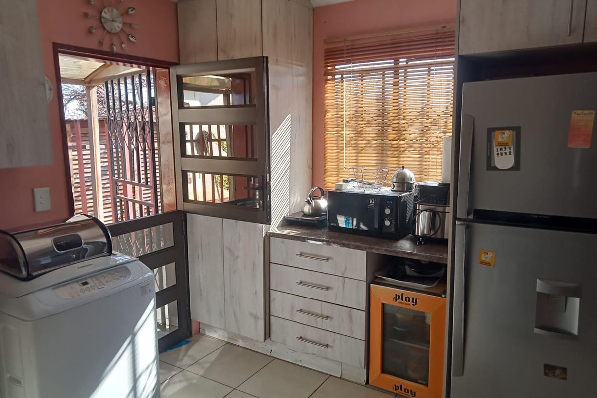 A functional kitchen area featuring built-in cabinetry, laminate countertops, tiled flooring, and direct access to the exterior through a security gate.