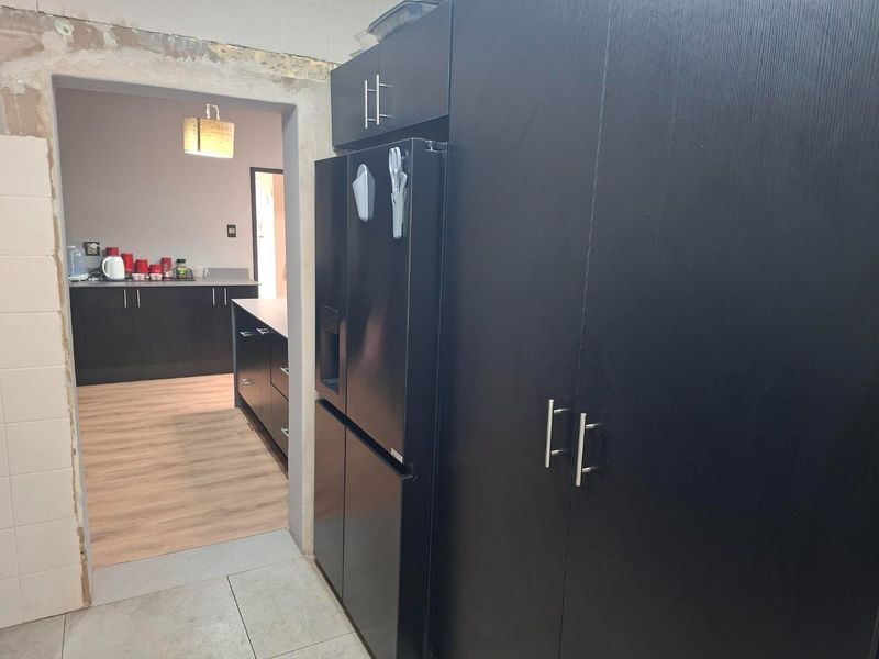 A scullery area featuring dark built-in cabinetry and a transition to an adjacent kitchen space, currently showing unfinished wall plastering around the doorway.