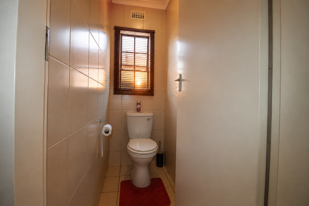 A compact, fully tiled guest toilet featuring a standard porcelain toilet suite and a small window with wooden blinds.