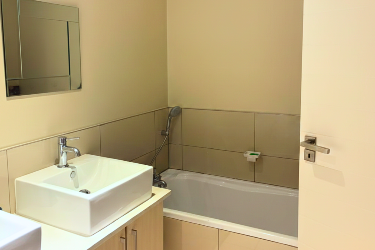A clean, modern bathroom featuring a white vessel sink, vanity cabinetry, a bathtub with a handheld shower attachment, and a wall-mounted mirror.